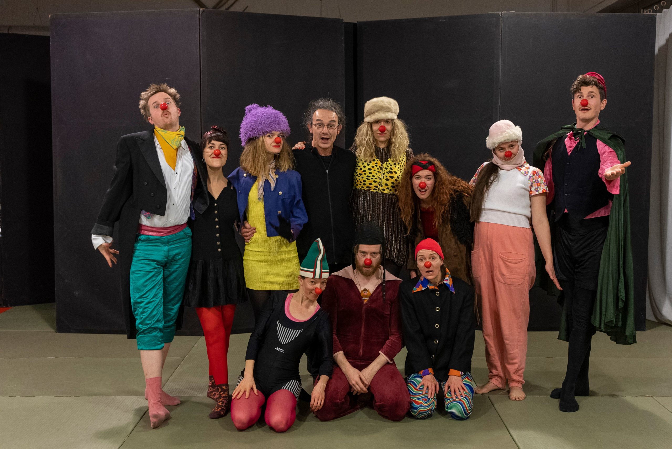 Mixed group of actors onstage wearing clown outfits and red noses