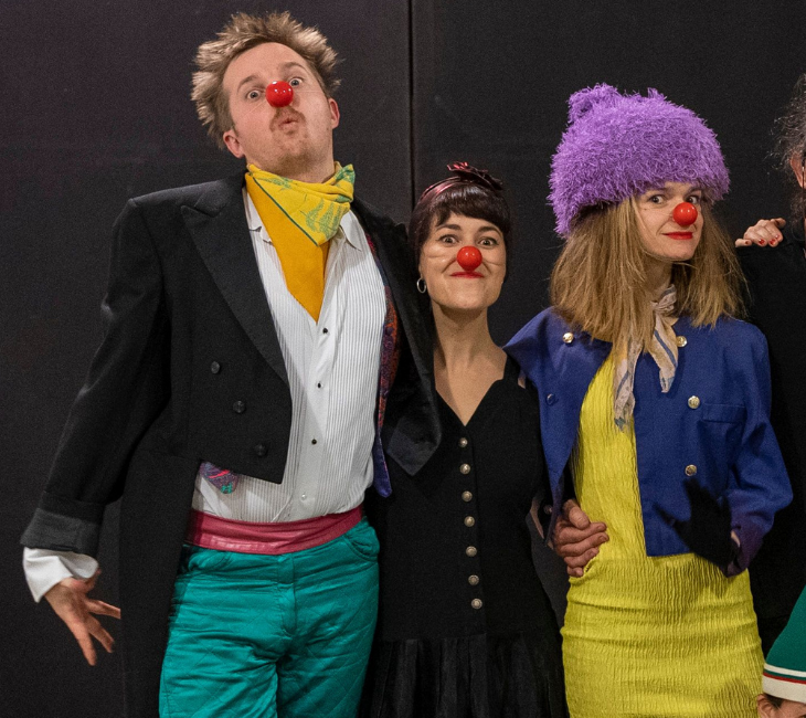 Mixed group of actors onstage wearing clown outfits and red noses