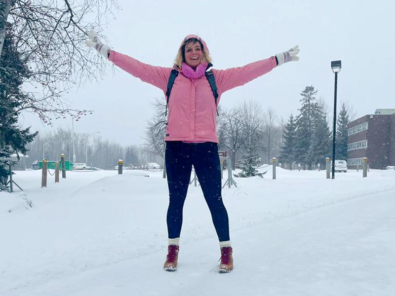 Erica Capecchi smiling with outstretched arms in the snow at Lakehead University Thunder Bay Campus